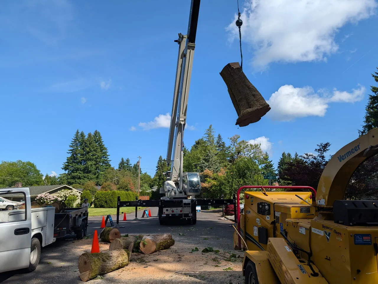 Crane hoisting a large log section above the worksite during a tree removal in Vancouver, WA