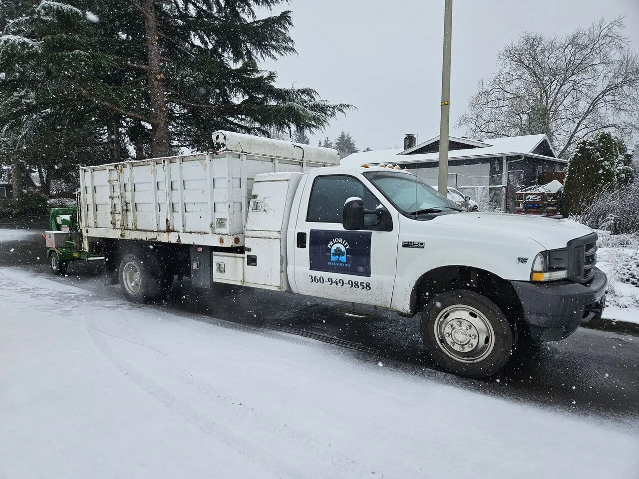 Priority Tree Service dump truck hauling debris through falling snow for a Clark County, WA homeowner