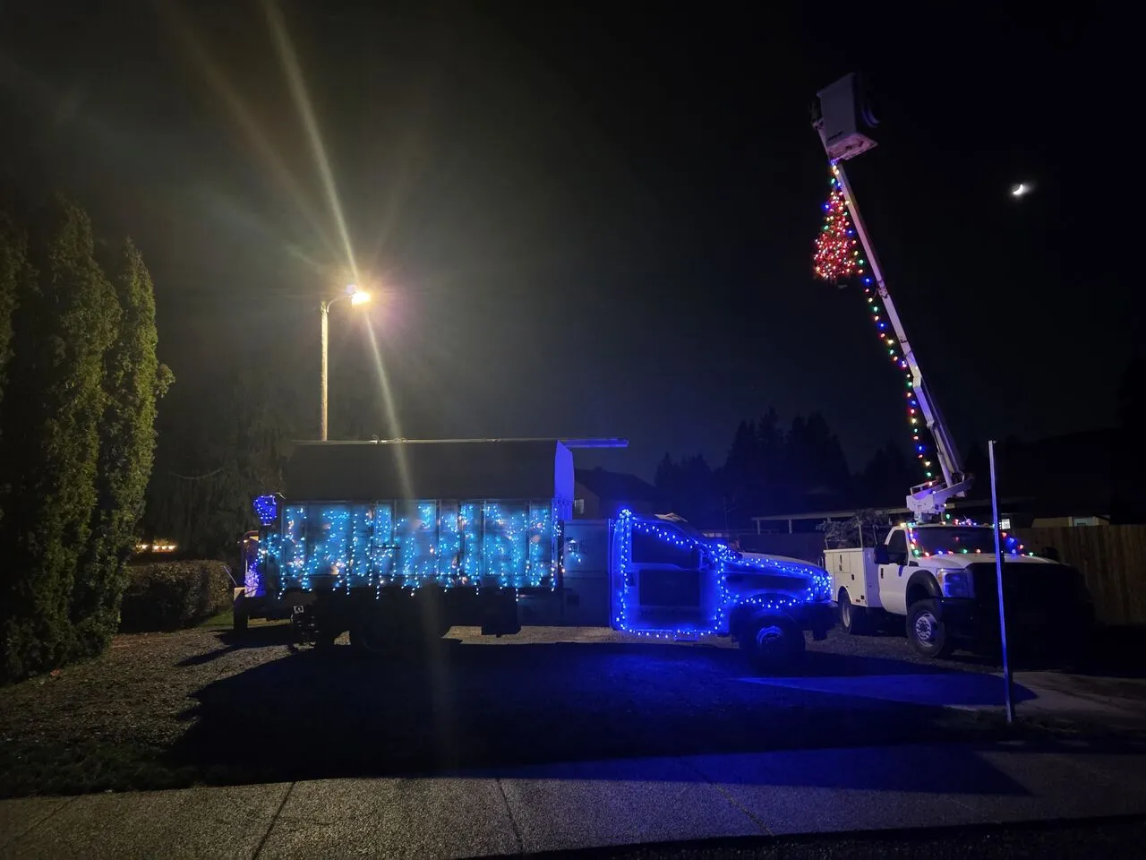 Bucket truck and chip truck decorated with holiday lights at night in La Center, WA