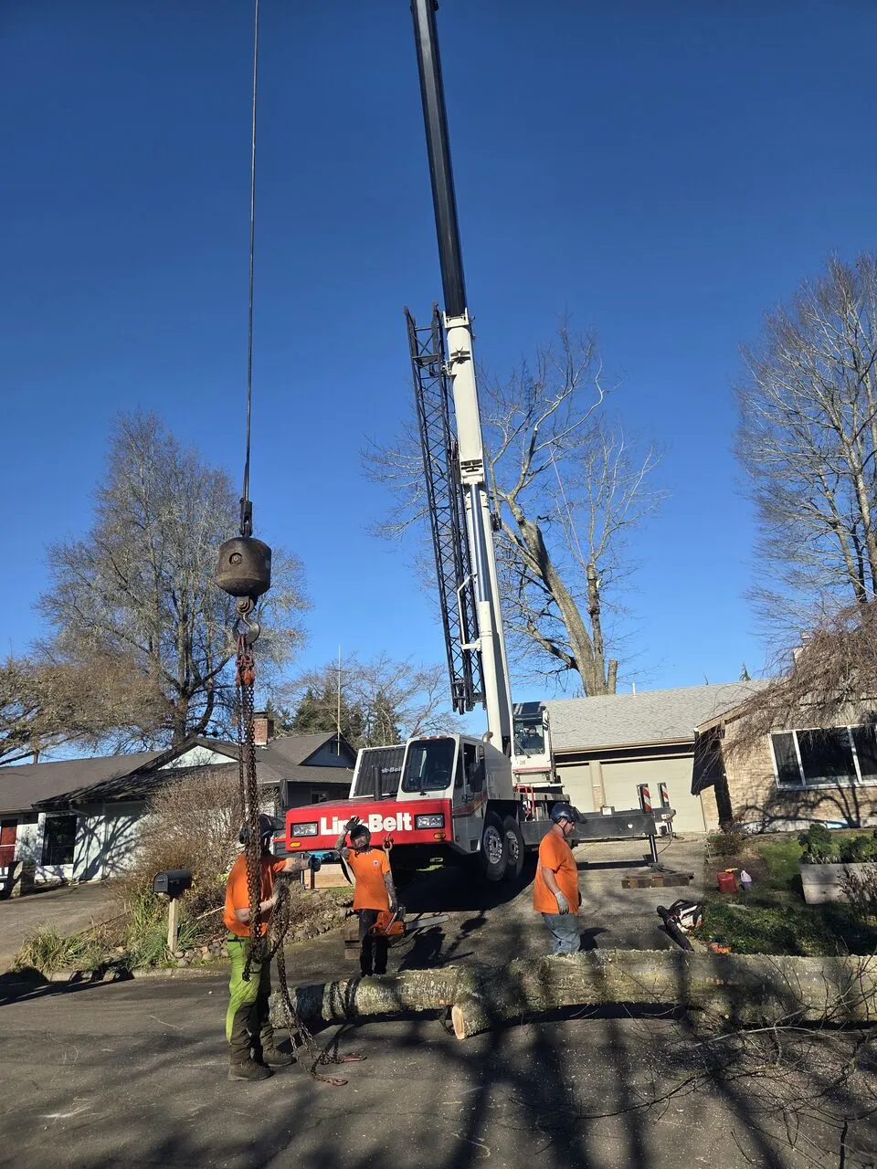 Ground crew rigging a fresh log section under a crane at a Salmon Creek, WA property