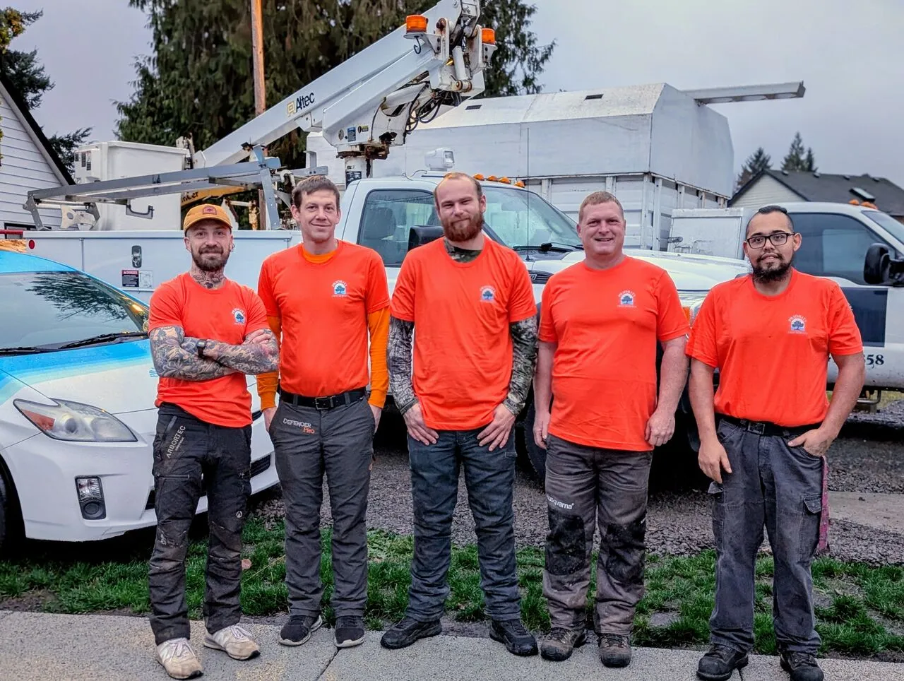 The Priority Tree Service crew in orange shirts posing by their bucket trucks in Hockinson, WA