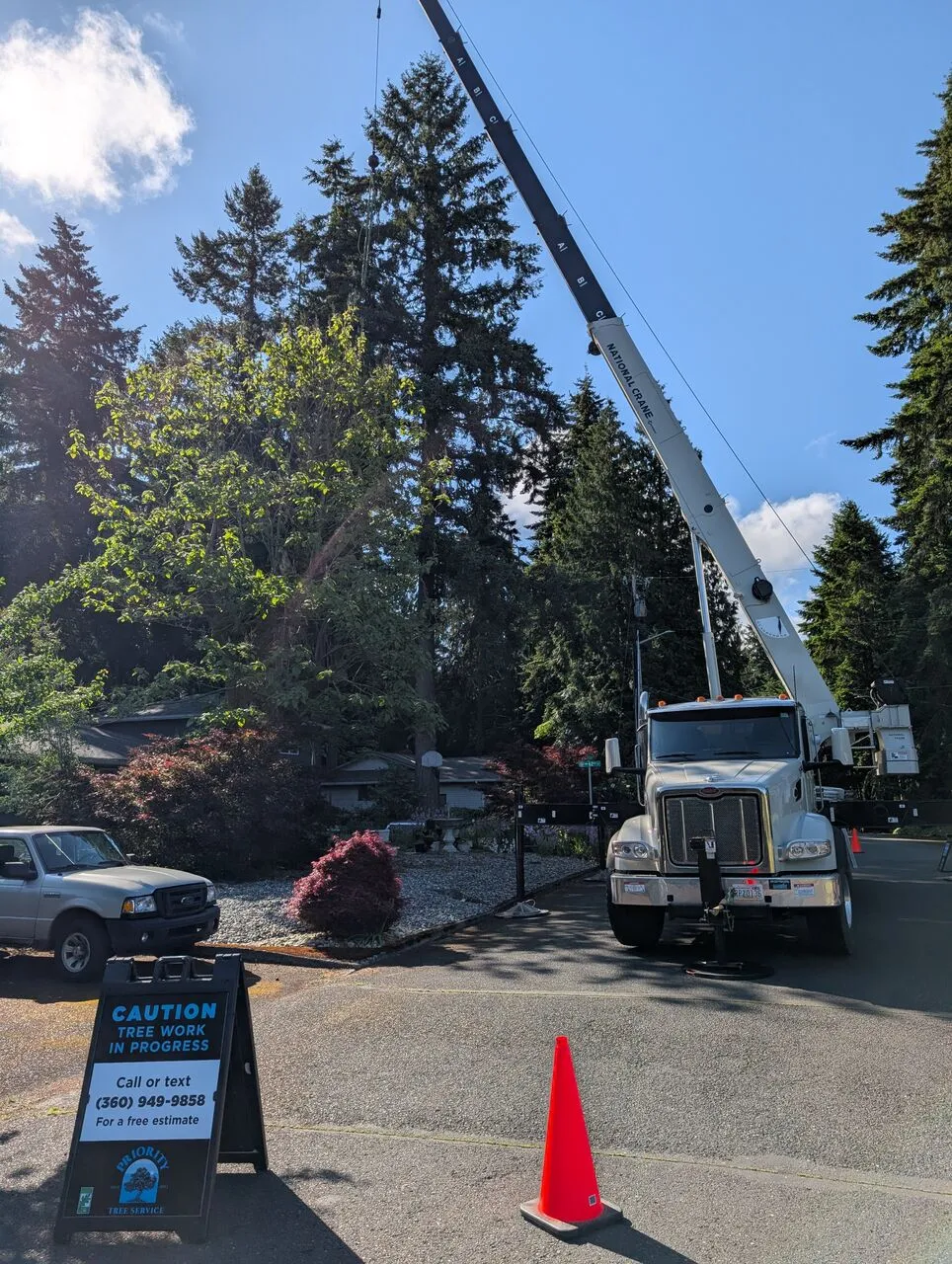 Crane truck and Priority Tree Service caution sign set up for tree work along a wooded street in Orchards, WA