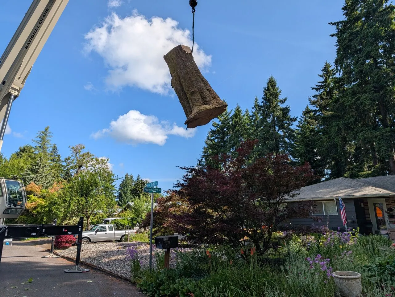 Crane hoists a heavy log over a residential yard during tree removal in Vancouver, WA